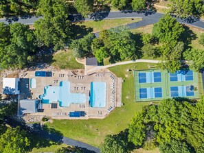 Vista aérea de un resort con piscina, canchas de tenis y zona de estacionamiento.