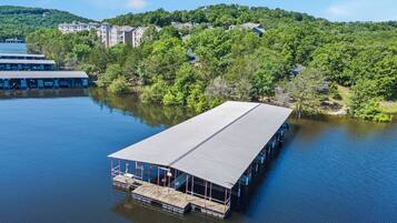 Een drijvende constructie met een overdekt terras, omgeven door rustig water, met gebouwen en bomen op de achtergrond.