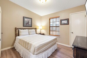 A bedroom with a bed, a nightstand, a lamp, a framed picture of an elk, a framed picture of a duck, and a door.