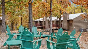Ein Campingplatz mit grünen Adirondack-Stühlen, die um eine zentrale Feuerstelle angeordnet sind, umgeben von Bäumen mit Herbstlaub.