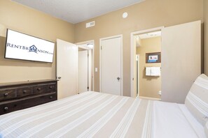 A hotel room with a bed, a dresser, a wall-mounted TV, and a door leading to a bathroom.