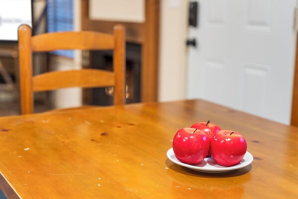 Una mesa de madera con un plato blanco que contiene tres manzanas rojas.