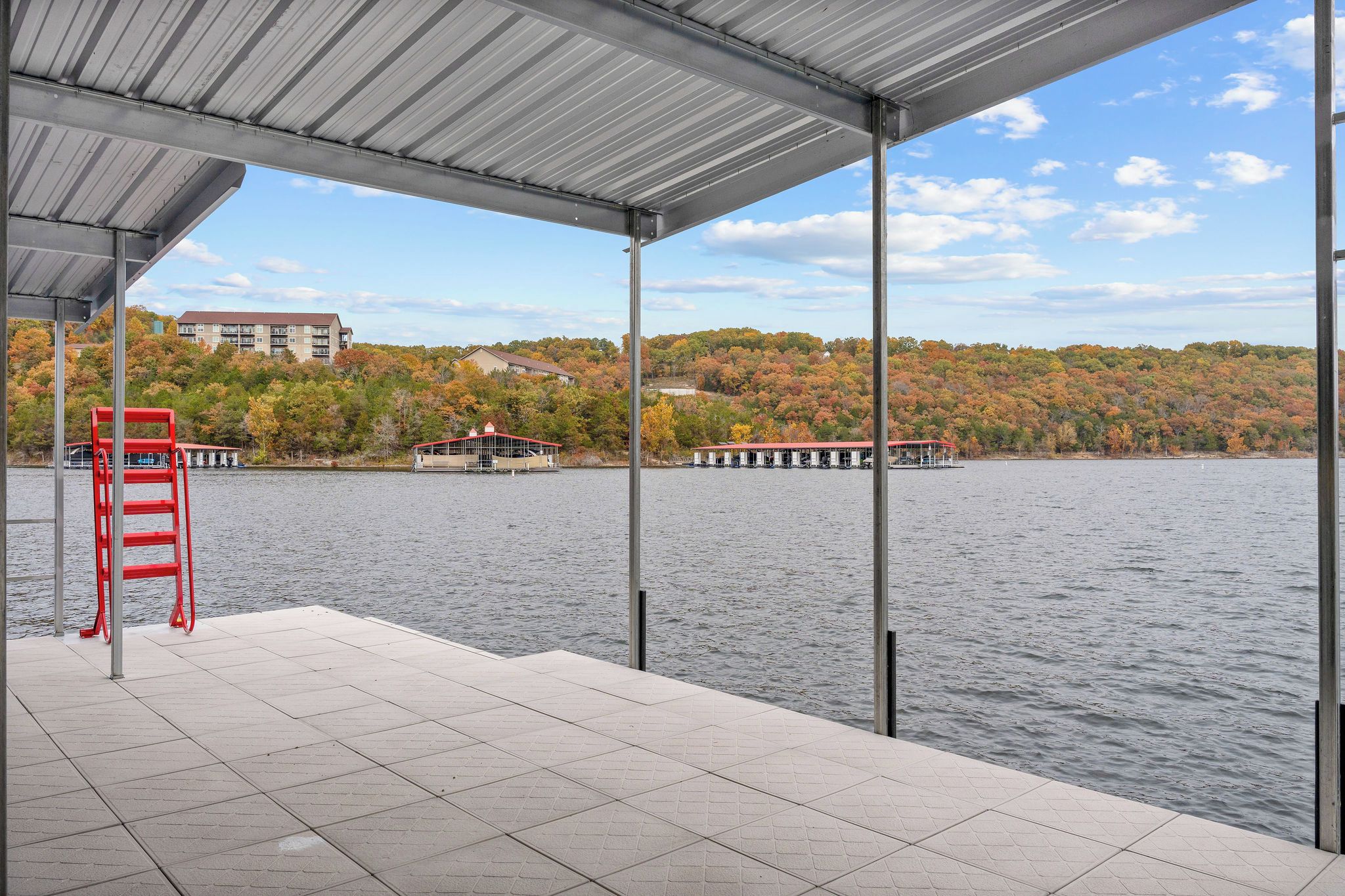 Un espace extérieur abrité avec vue sur un lac, une chaise rouge et des bâtiments en arrière-plan.
