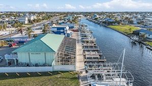 A marina with boats docked along a narrow waterway, surrounded by residential buildings and a large green-roofed structure labeled "BUCCANEER". - 1/1 Condo in St. James City! Boat Slip Included! (Saint James City)