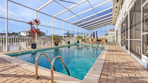 A covered swimming pool with a clear view of the ocean, surrounded by potted plants and a white fence. - 1/1 Condo in St. James City! Boat Slip Included! (Saint James City)