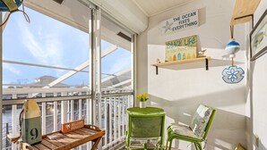 A balcony with a wooden table, a green chair, and a decorative item. There are two wall-mounted signs, one with a starfish and the other with a flower. - 1/1 Condo in St. James City! Boat Slip Included! (Saint James City)