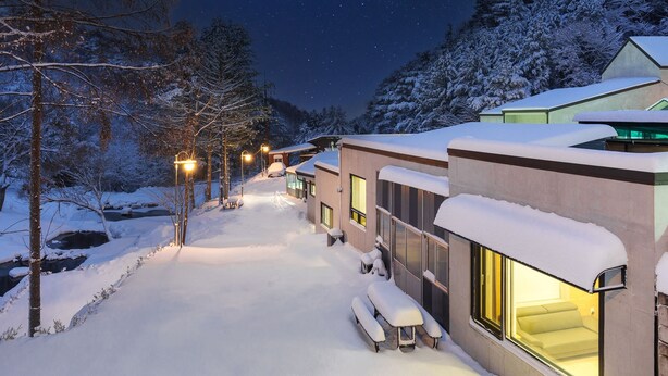 Een met sneeuw bedekte pad dat leidt naar een rij moderne gebouwen met grote ramen en terrasjes.