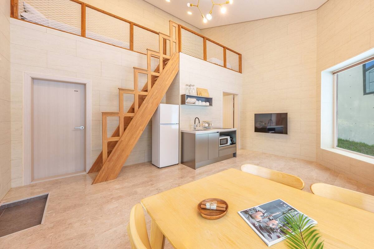 Eine moderne Küche mit eingebautem Ofen, Mikrowelle und Spüle, einer Holztreppe sowie einem Essbereich mit Tisch und Stühlen.