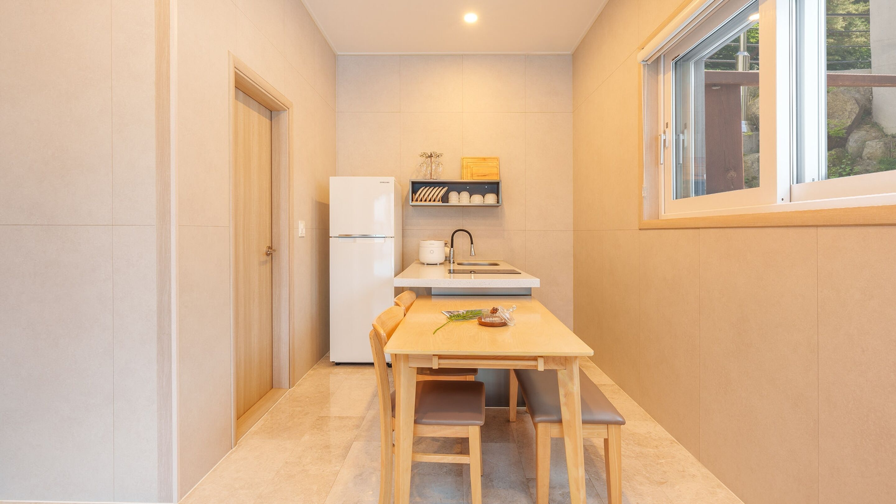 A compact kitchen with a refrigerator, a sink, and a small dining table with chairs.