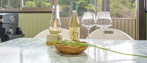 A table with a bottle of wine, two glasses, a candle, and a basket of green leaves.