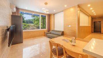 Una cocina moderna con refrigerador integrado, una mesa de comedor con sillas, un sofá y un amplio ventanal con vistas al verdor.