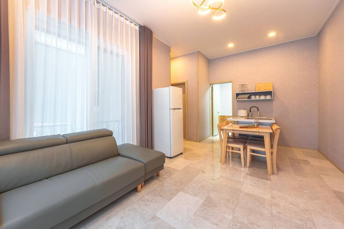 Ein modernes Wohnzimmer mit einer Couch, einem Essbereich mit Tisch und Stühlen, einem Kühlschrank und einer Küchenzeile mit Spüle und Schränken.