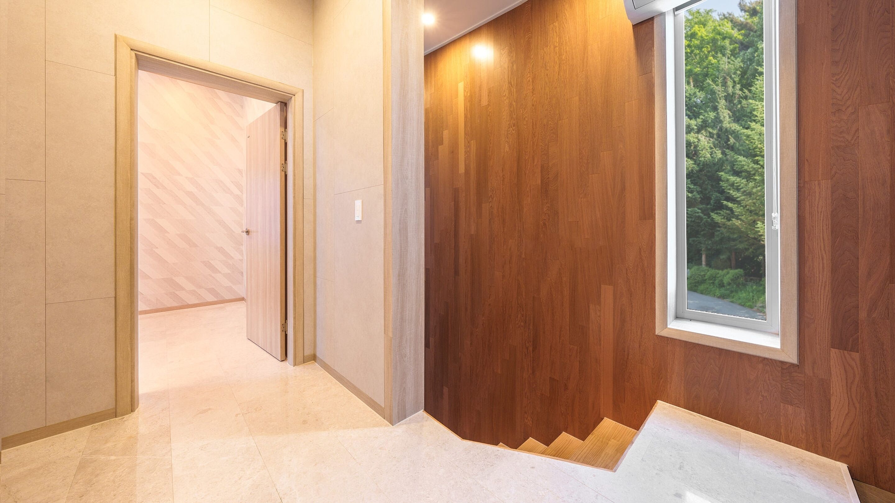 Un interior moderno con una escalera de madera, una puerta que da a otra habitación y una ventana con vistas a zonas verdes.