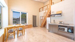 Een moderne keuken met een ingebouwde oven, een magnetron en een spoelbak. Er is een eethoek met een tafel en stoelen, en een trap die naar een bovenverdieping leidt.