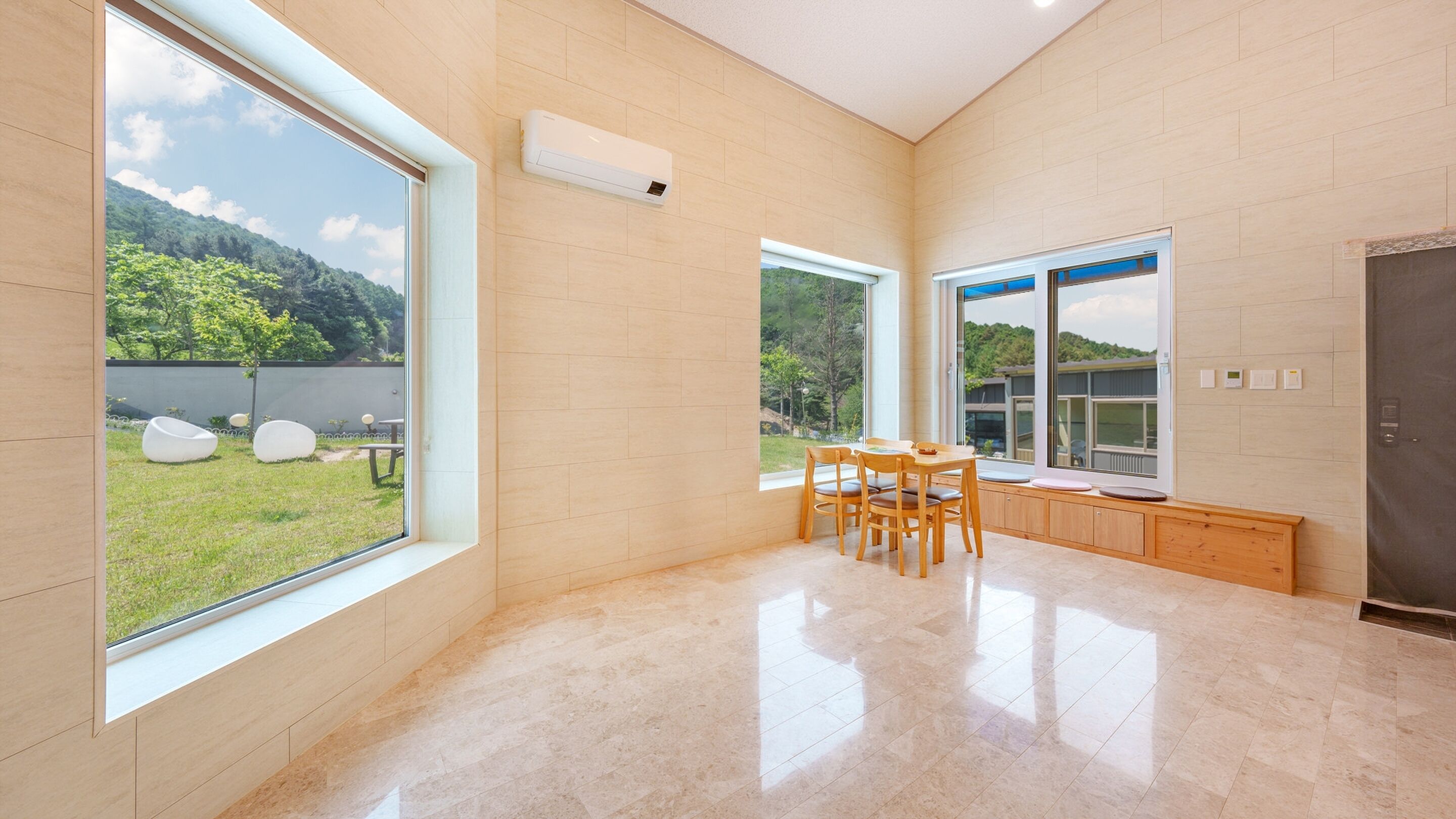 Cocina amplia con ventanas grandes, zona de comedor con mesa y sillas, y vista a un paisaje verde.