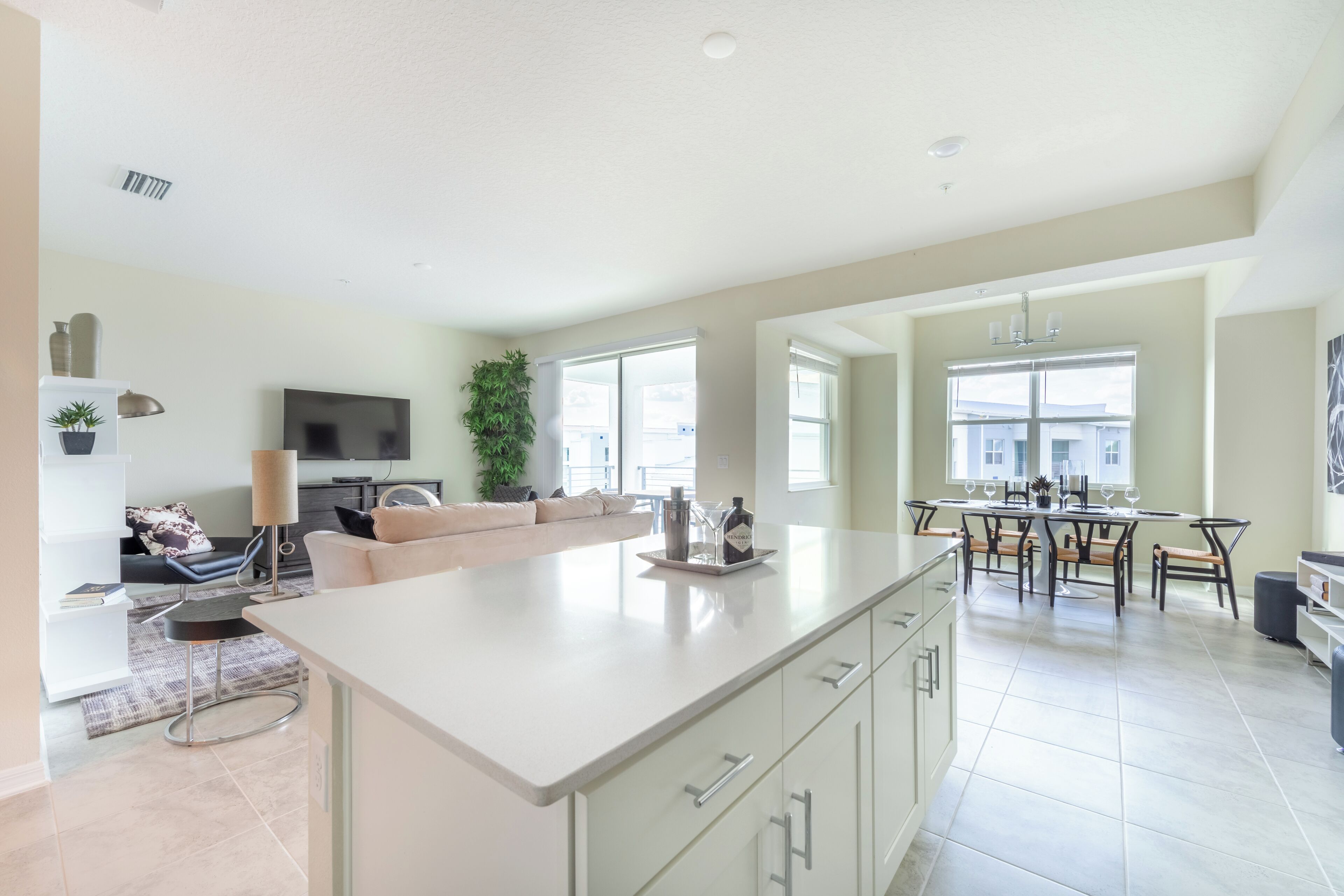 A spacious kitchen with a large island, a dining area with a table and chairs, a living area with a sofa and TV, and a kitchen counter with cabinets.