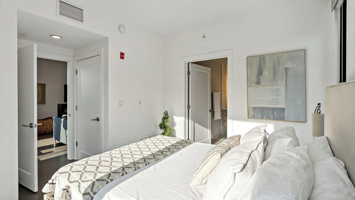 A hotel room with a large bed, a small plant, and a painting on the wall.