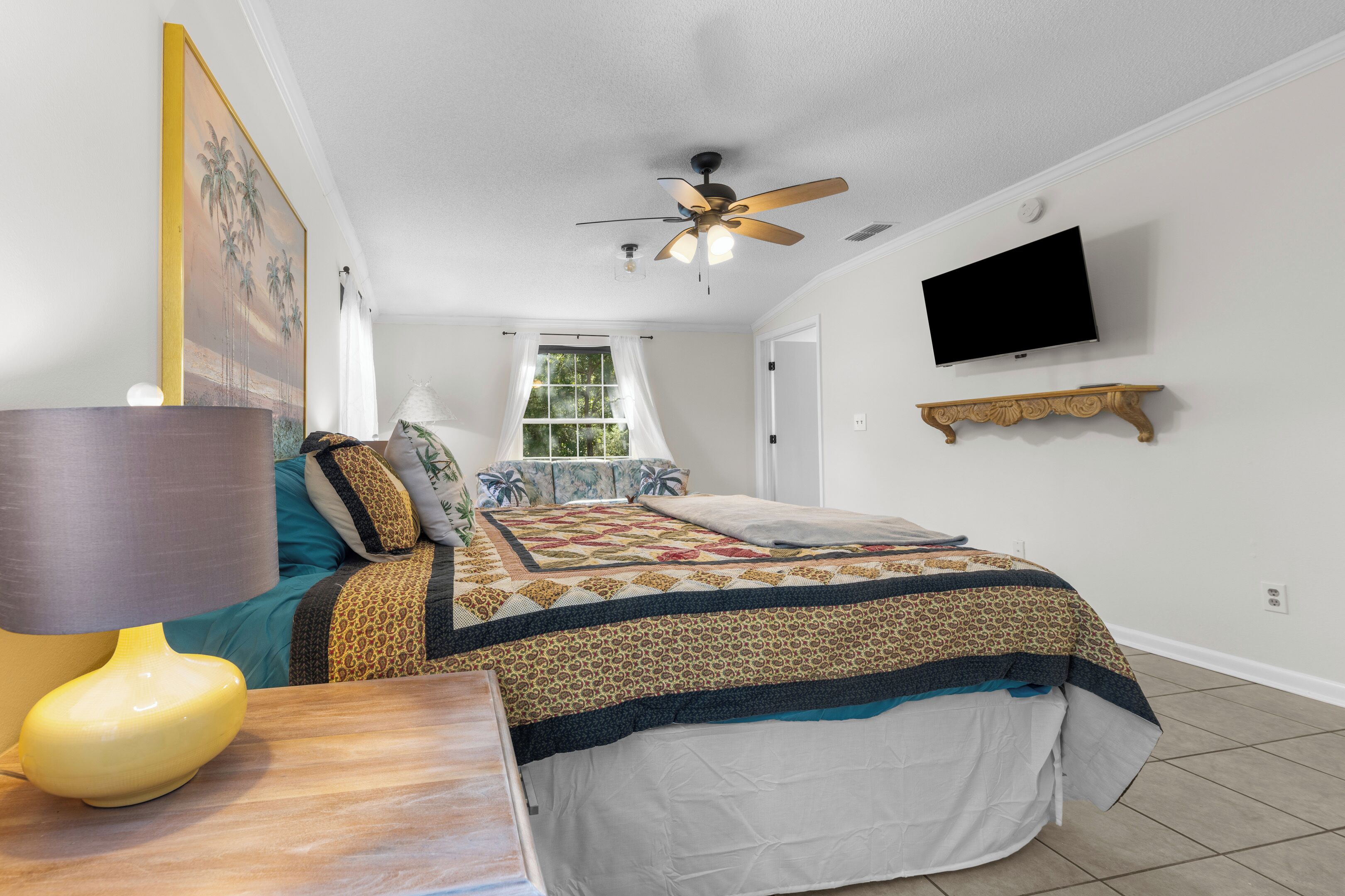 A bedroom with a bed, a ceiling fan, a TV, and a window with curtains.