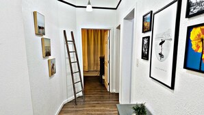 A hallway with wooden flooring, white walls, and framed pictures. A ladder leans against the wall, and a plant is on a table. - Grand Victorian in Mansion Flats - 3BR/1.5BA (Sacramento)