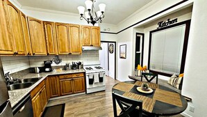 A kitchen with wooden cabinets, a stove, a sink, and a dining area with a table and chairs. - Grand Victorian in Mansion Flats - 3BR/1.5BA (Sacramento)
