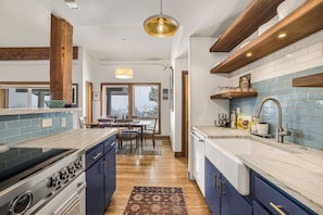 A kitchen with a stove, sink, and wooden beams, leading to a dining area with a table and chairs.