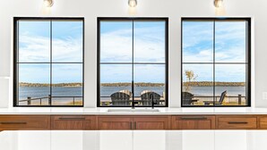 Eine Küche mit einem großen Fenster und Blick auf einen See, ausgestattet mit einer Holzausstattung und einem Spülbecken.