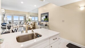 A modern kitchen with a marble countertop, stainless steel sink, and a dining area with a sofa and chairs.