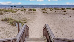 A beach path leading to the ocean with a wooden fence and a clear view of the sea.