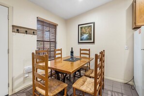 Un comedor con mesa y sillas de madera, una ventana con persianas, un cuadro en la pared y un refrigerador.