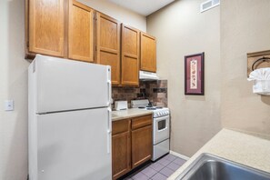 Una cocina compacta con armarios de madera, un refrigerador blanco, estufa y lavamanos.