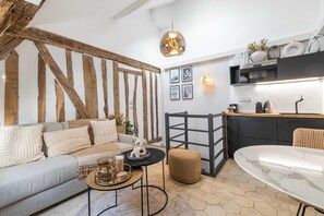 Un salon moderne comprenant un canapé, une table basse et un pouf, un coin cuisine avec une table à manger, et un luminaire suspendu.