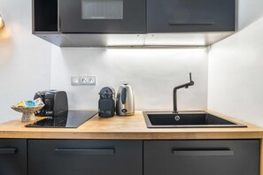 Cozinha moderna com bancada preta, chaleira, cafeteira e pia.