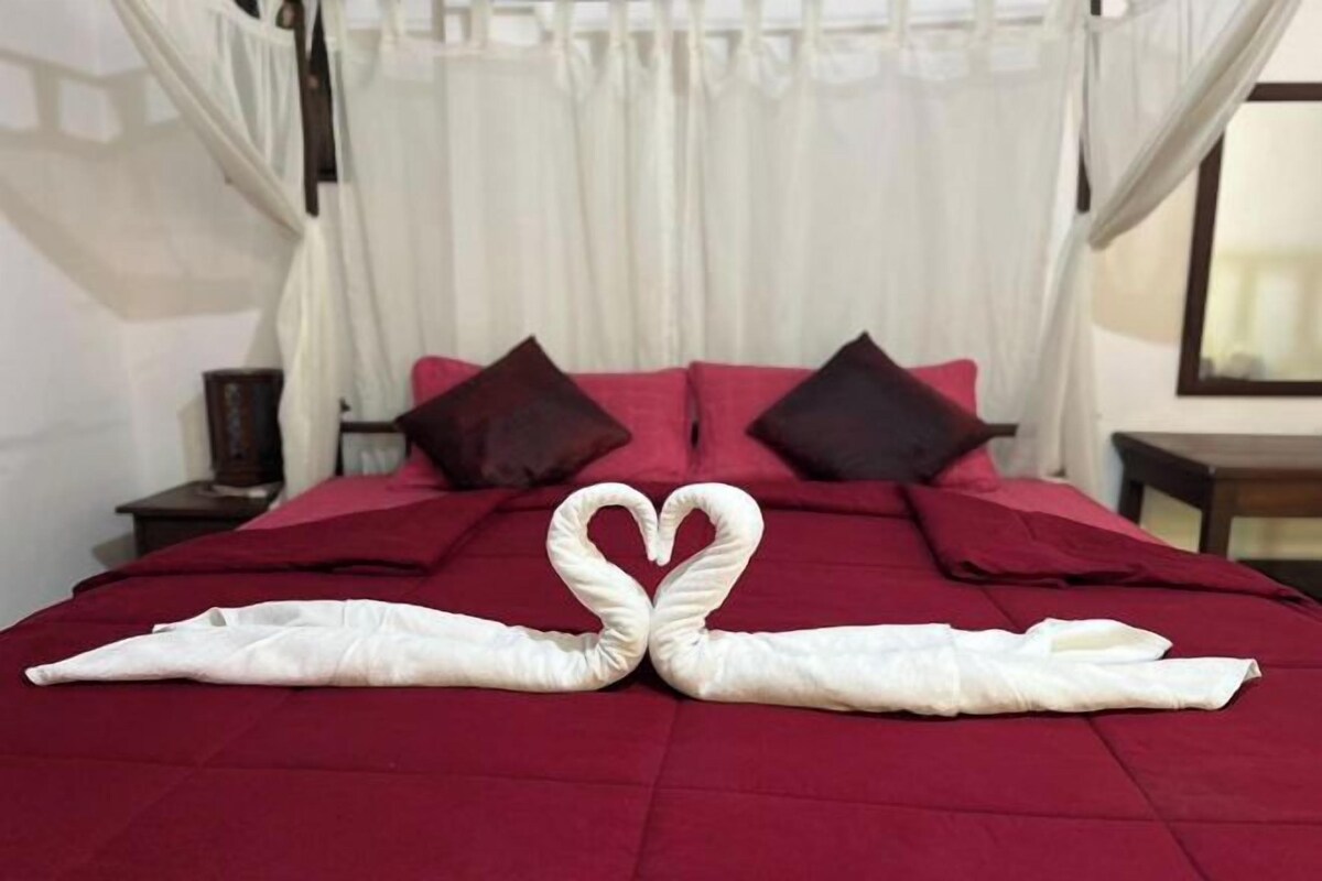 Een bed met een rode sprei, twee kussens en een hemelbed.