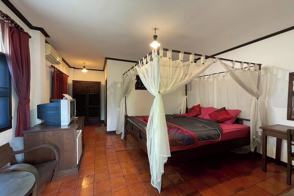 A bedroom with a four-poster bed, a small desk with a television, and a window with curtains.