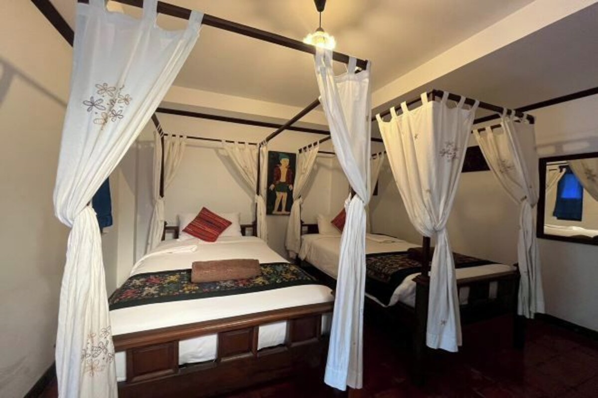 Une chambre avec un lit à baldaquin, deux lits simples et une table de chevet.