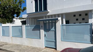 Un edificio moderno con fachada blanca, una reja azul y un coche rojo estacionado adelante.