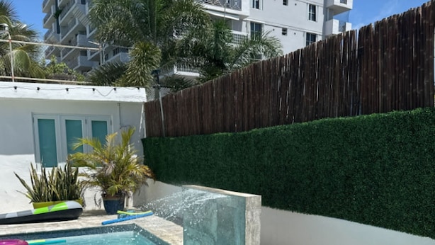 Una piscina con agua cristalina azul, rodeada por un muro blanco y una cerca de madera.