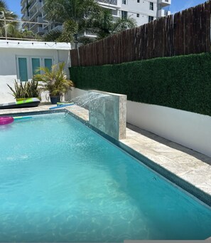 A swimming pool with clear blue water, surrounded by a white wall and a wooden fence. - Otium Vacation Rental With Pool Steps From The Beach Parking Pet Friendly (San Juan)