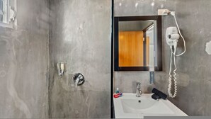 Un baño con ducha, lavamanos, espejo y secador de pelo en la pared.