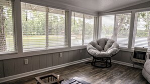 Una habitación con ventanas amplias, un sillón acolchado, una mesita pequeña y un radiador.