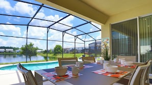A dining area with a glass enclosure overlooking a swimming pool and a lake, featuring a table set with bowls and cups. - Pool Villa, Game Room, Theater, 20 Minutes to Disney, Great Pool Heat (Kissimmee)