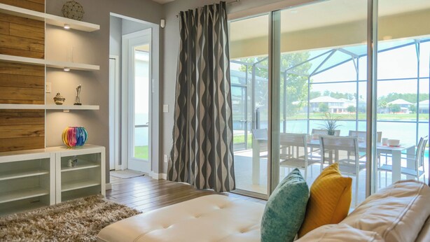 A modern living room with a sofa, a patterned curtain, and a view of an outdoor patio area. - Pool Villa, Game Room, Theater, 20 Minutes to Disney, Great Pool Heat (Kissimmee)