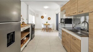 A modern kitchen with a stainless steel refrigerator, wooden cabinets, and a dining area with a white table and chairs.