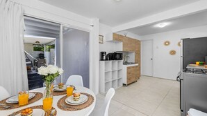 A modern kitchen with a refrigerator, stove, and wooden cabinets. There is a dining area with a table set for two, featuring plates, glasses, and a vase with flowers.