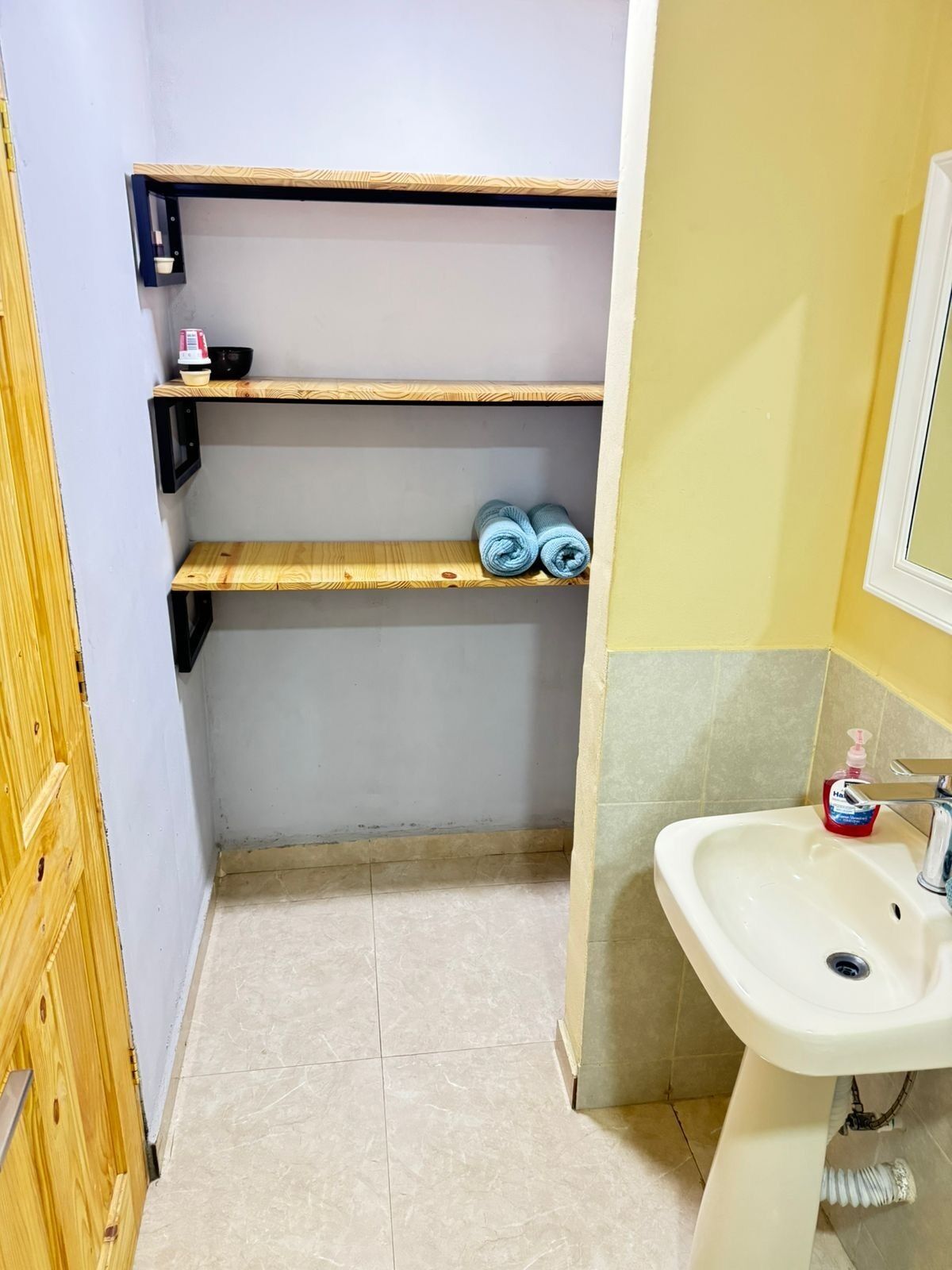 A bathroom with a white sink, a mirror, and wooden shelves.