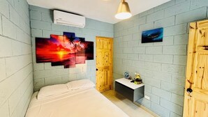A bedroom with a bed, a wooden door, a small table with a lamp, and a wall-mounted air conditioner.