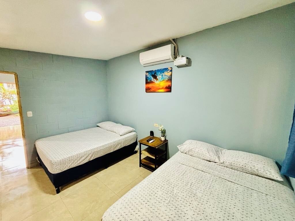 A room with two beds, a small table with a plant, and an air conditioning unit on the wall.