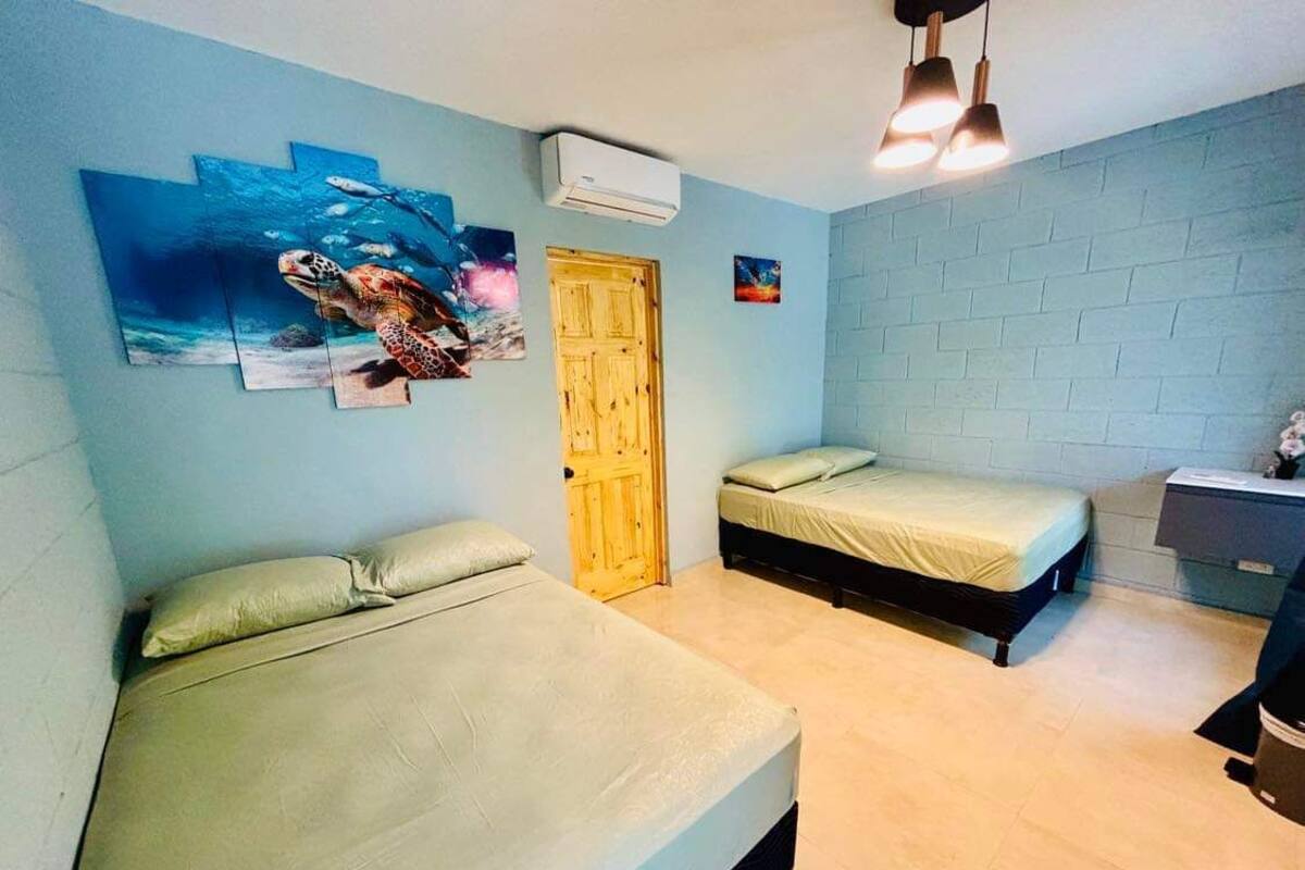 A room with two beds, a wooden door, and a wall-mounted air conditioner.