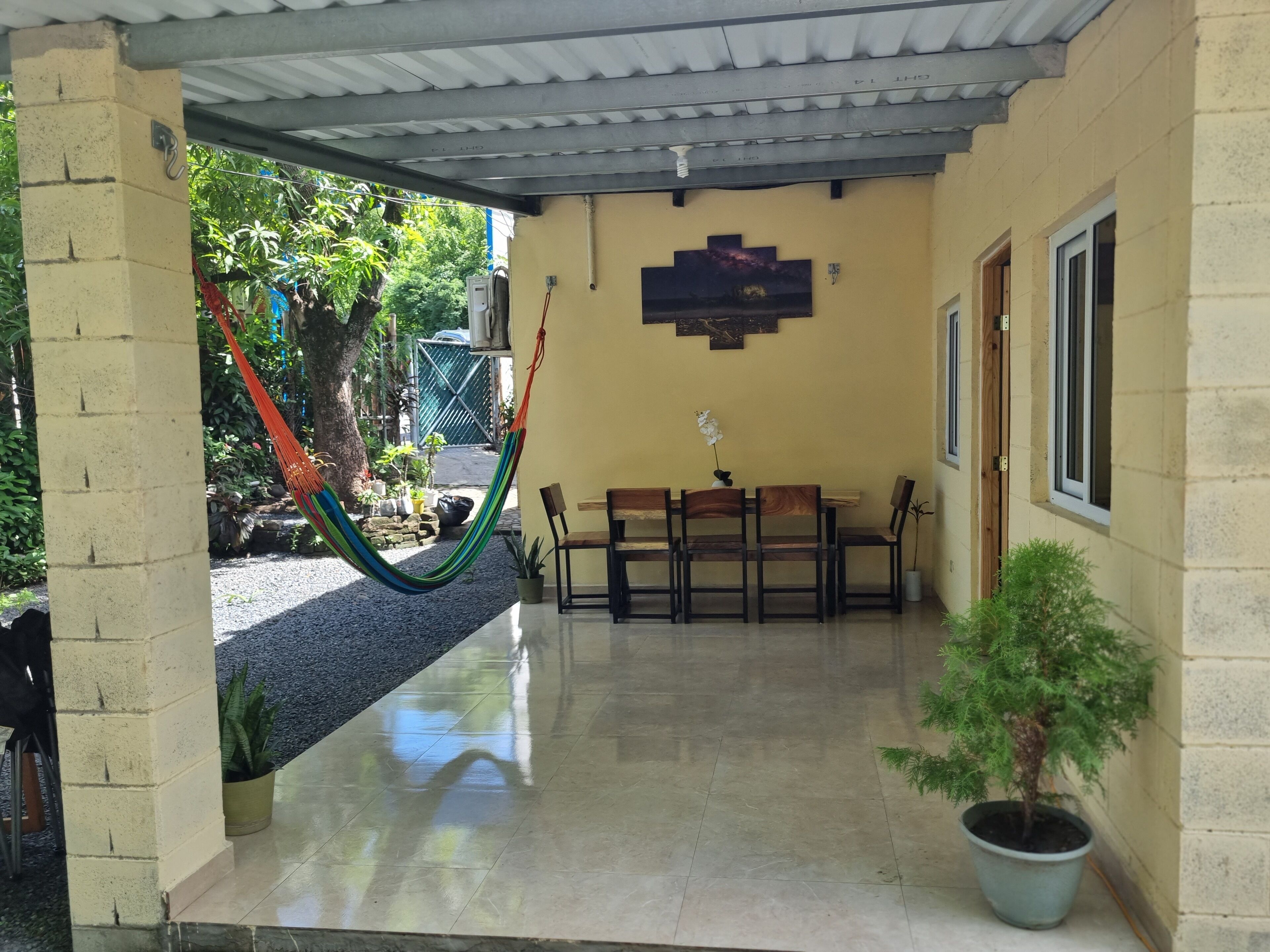 Ein überdachter Patio-Bereich mit einer Hängematte, einem Holztisch mit Stühlen und Kübelpflanzen.