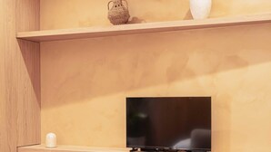 A modern living room with a flat-screen TV on a wooden shelf, a small decorative vase, and a woven basket. - Charming Studio With A/C - 2P - Center St Tropez (Saint-Tropez)
